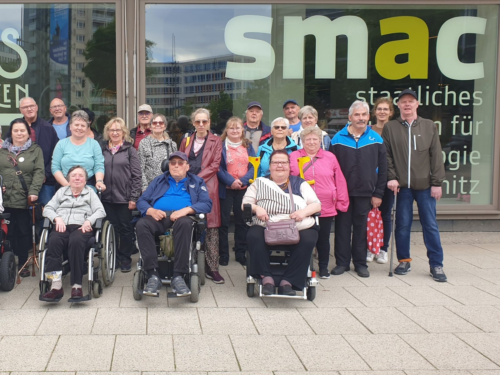 Gruppenfoto von Vereinsmitgliedern, einige im Rollstuhl, vor einem Museum